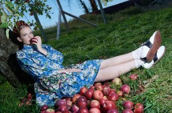 Batsheva Hay eating apples under an apple tree wearing Mirfield print Carwyn Dress.