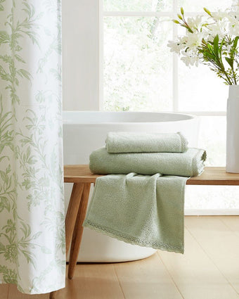 Juliette Lace Hem Green 3 Piece Towel Set Lifestyle view of folded towels on a bench