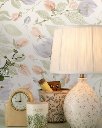 Orisia Peony Pale Sage Green Wallpaper on a wall behind a clock, candle, pen holder and lamp