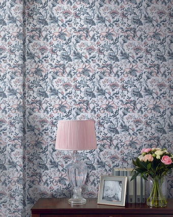 Portia Pale Slate Wallpaper on a wall behind a table with a lamp, frame and floral decor.