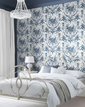 Tuileries Midnight Blue Wallpaper on a wall behind a metal bed with white bedding