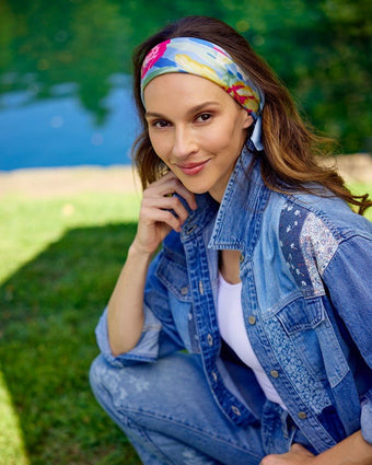 Tulip Scarf on a model worn as a headband. The model is wearing a denim shirt, jeans and white tank top standing outside under greenery.