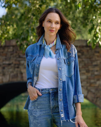 Tulip Scarf tied around neck on a model wearing a denim shirt, jeans and white tank top standing outside under greenery.