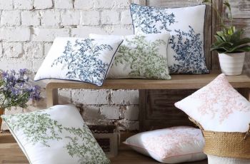 Bedford blue, pink and green print decorative cushions on a bench in front of a white brick wall.